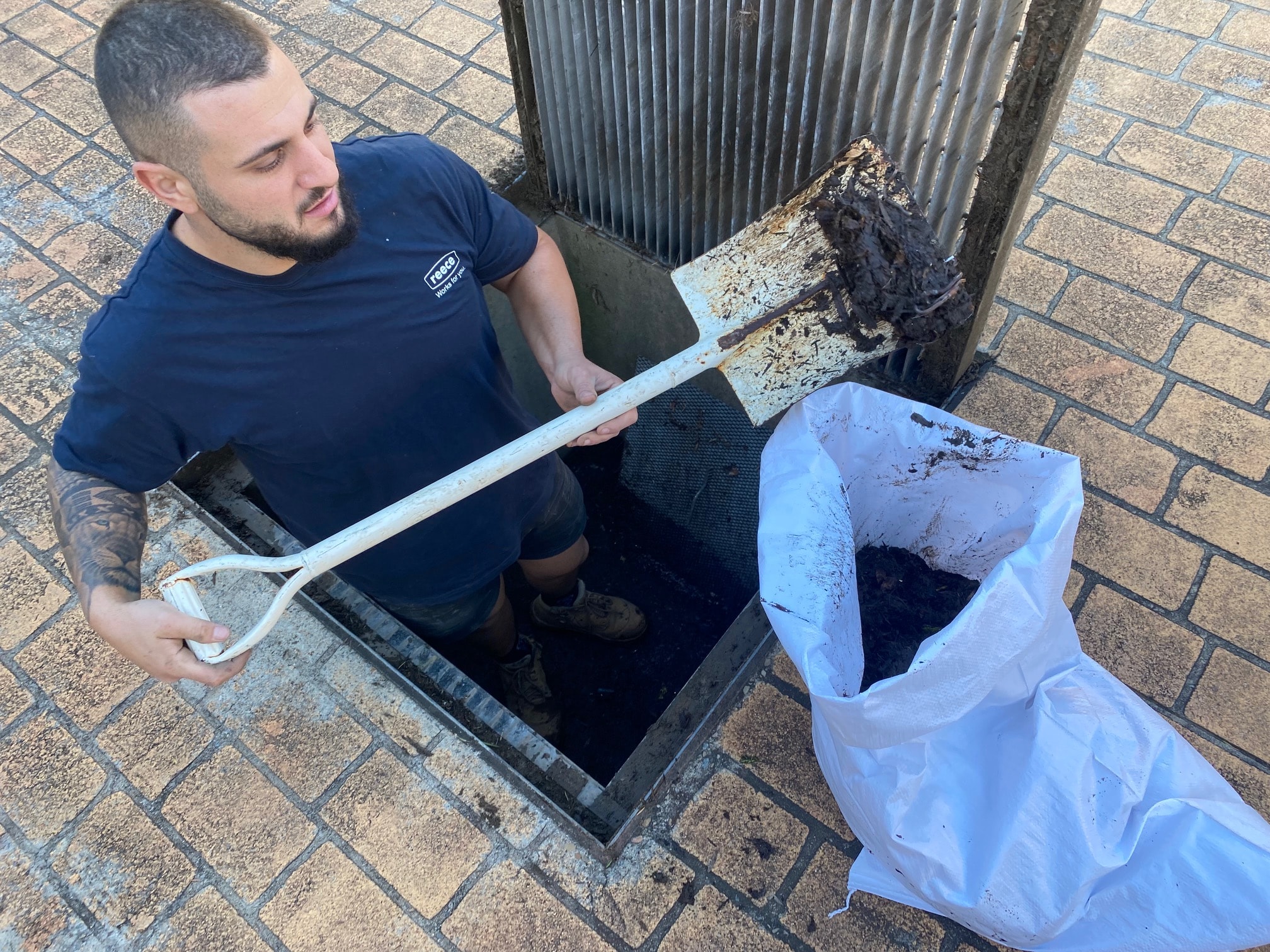 Plumber removing debris from blocked stormwater pit drain in driveway